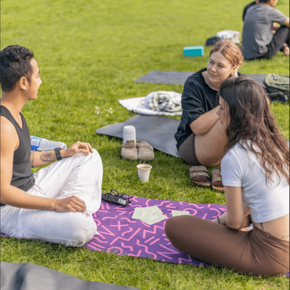 Three people playing a conversation card game outdoors sitting on colorful mats on grass