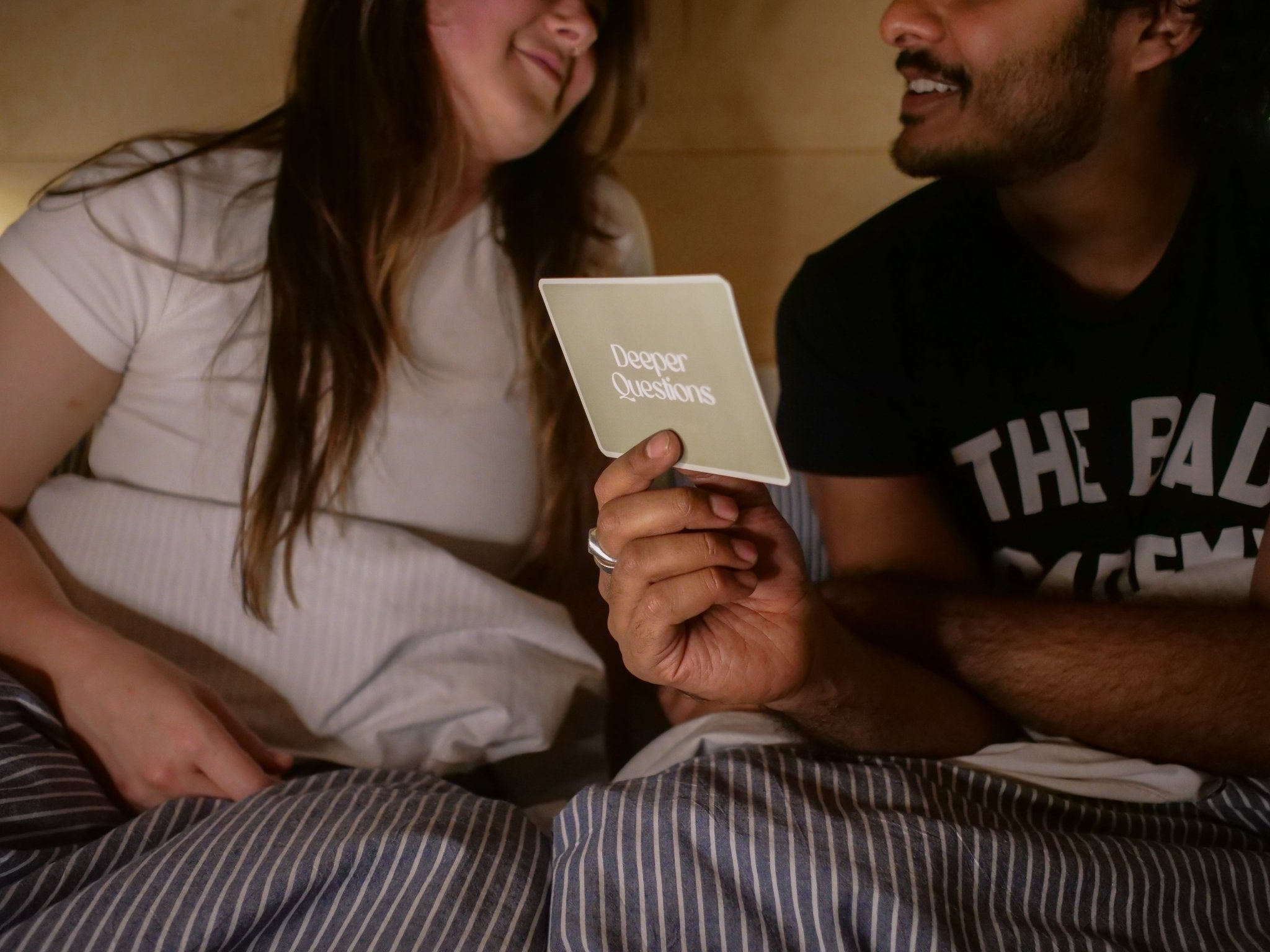 Couple playing Deeper Questions conversation card game while sitting together under a blanket